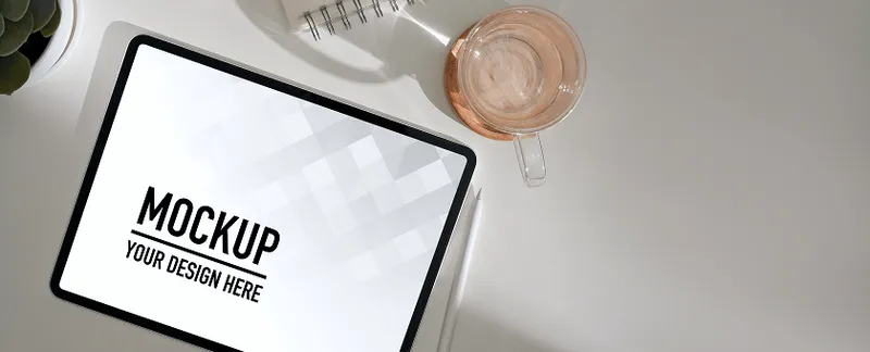 Tablet mockup lying flat next to a drink and saucer on a marble surface.